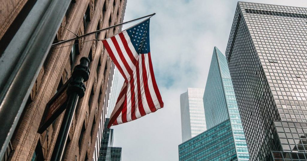 the-usa-or-united-states-of-america-flag-on-a-flagpole-near-skyscrapers-under-a-cloudy-sky(1)